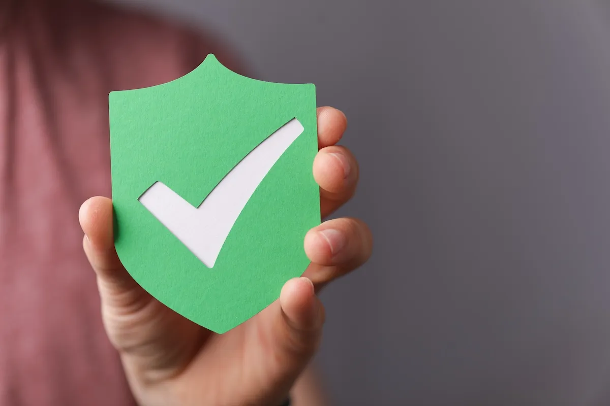 A person holds a green shield-shaped cutout with a white check mark in the center, symbolizing approval or security—an ideal image for websites for bookkeepers seeking to convey trust and reliability.