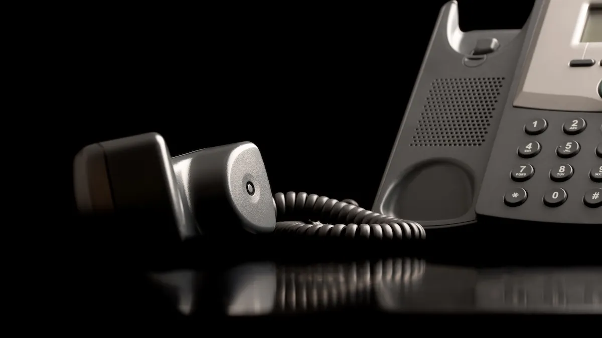 A corded office telephone with the handset resting off the hook, lying beside the main phone unit on a reflective black surface—perfect for businesses searching websites for bookkeepers.