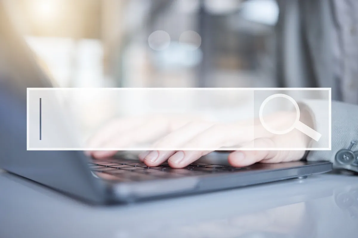 Hands typing on a laptop keyboard with a transparent search bar overlay, featuring a magnifying glass icon on the right—ideal for exploring websites for bookkeepers.